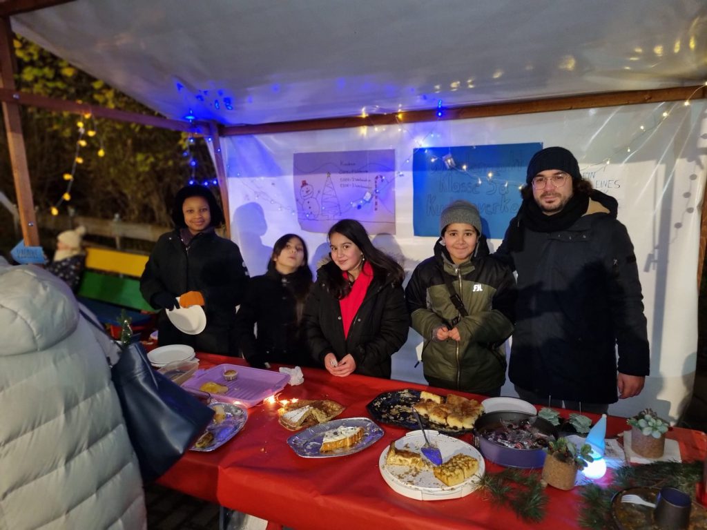 Schüler mit Erwachsen beim Kuchenverkauf am Weihnachtsmarkt im Dezember 2022